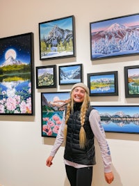 a woman standing in front of framed paintings in an art gallery