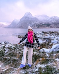 a woman in a pink scarf standing in front of a mountain